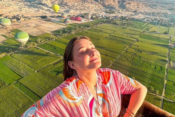 A person standing in a hot air balloon aloft over a green field