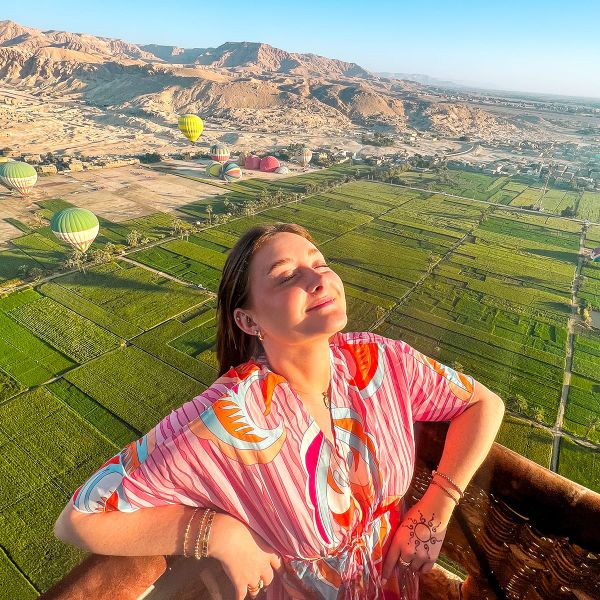 A person standing in a hot air balloon aloft over a green field