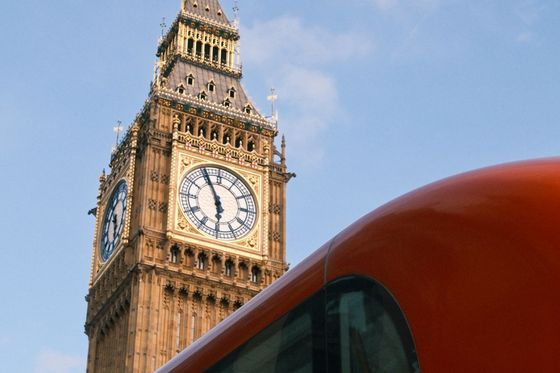 Clock tower with ornate details against a blue sky, partially obscured by a red bus.