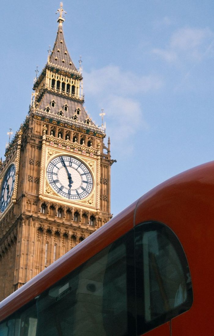 Clock tower with ornate details against a blue sky, partially obscured by a red bus.