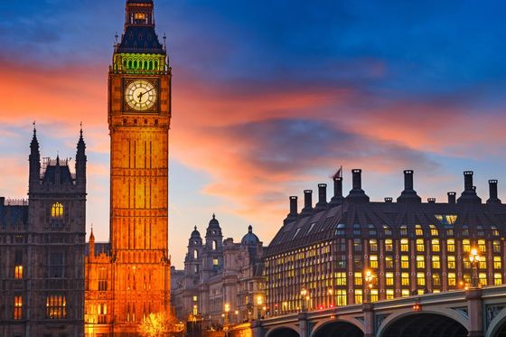 Big Ben at sunset with a colorful sky, reflected in the River Thames, and Westminster Bridge lit by streetlights.