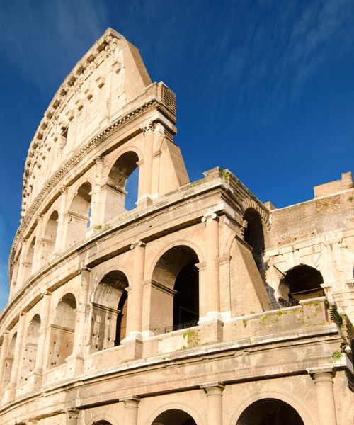 Close-up of the Colosseum in Rome against a clear blue sky, highlighting its ancient arches and worn stone exterior.