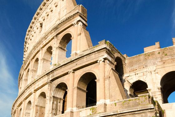 Close-up of the Colosseum in Rome against a clear blue sky, highlighting its ancient arches and worn stone exterior.