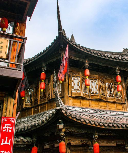 Traditional Chinese building with ornate wooden architecture, red lanterns, and intricate roof details against a blue sky.