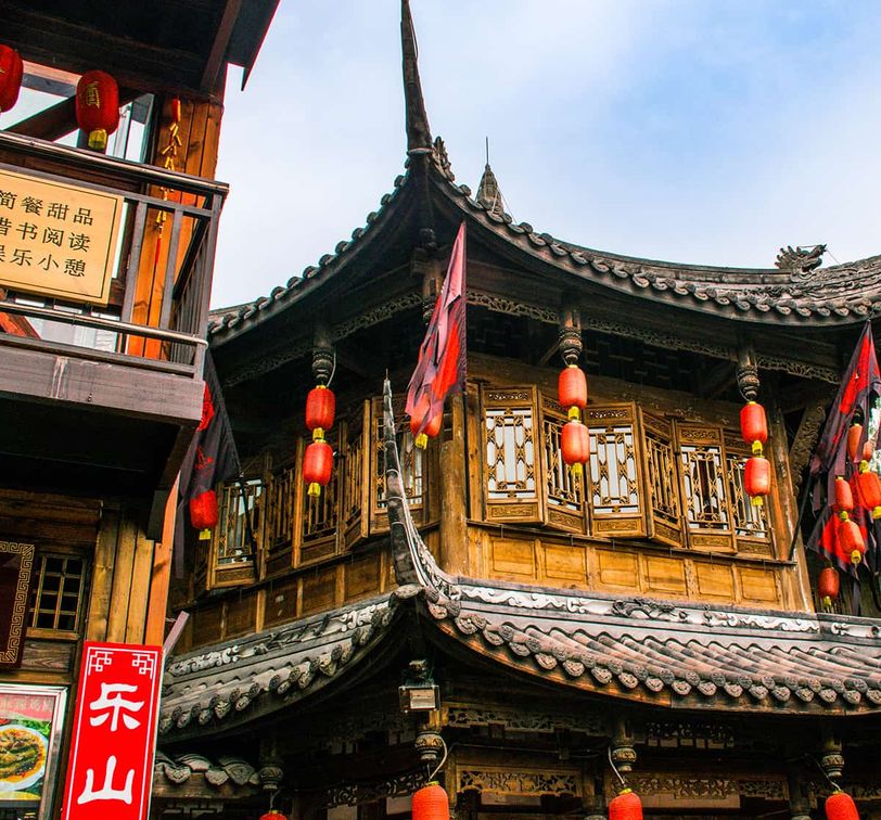 Traditional Chinese building with ornate wooden architecture, red lanterns, and intricate roof details against a blue sky.