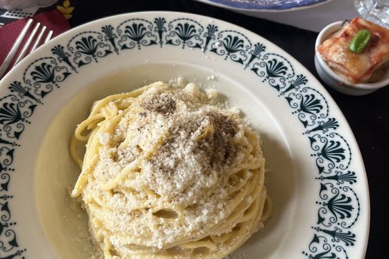 A plate of spaghetti topped with grated cheese and pepper, surrounded by other dishes, including appetizers and a small baked item with basil.