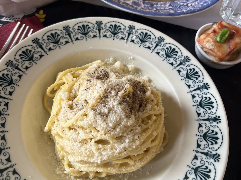 A plate of spaghetti topped with grated cheese and pepper, surrounded by other dishes, including appetizers and a small baked item with basil.