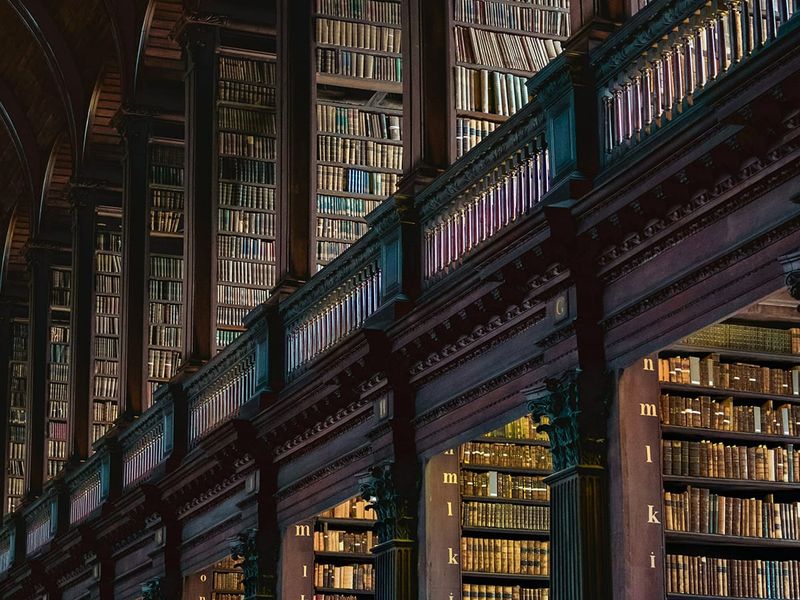 A grand library interior with tall wooden shelves filled with numerous books, ornate columns, and soft lighting creating a warm ambiance.