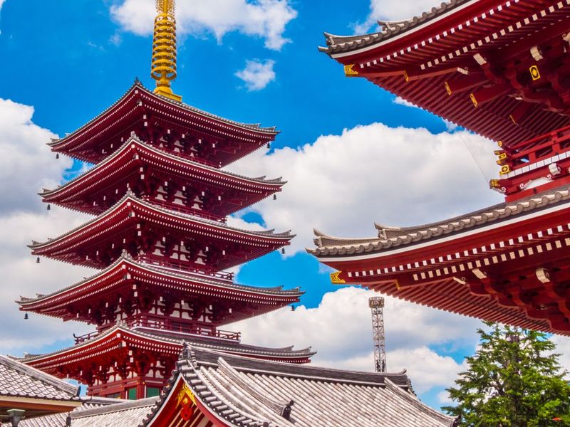 A five-story red pagoda with ornate roofs against a bright blue sky with fluffy white clouds.