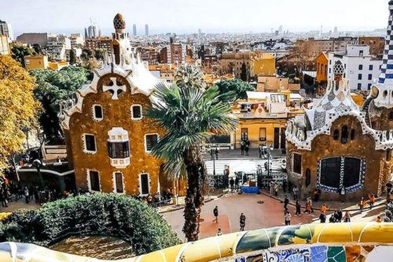 Colorful mosaic tiles and whimsical buildings in Park Güell, Barcelona, with a cityscape view in the background under a partly cloudy sky.
