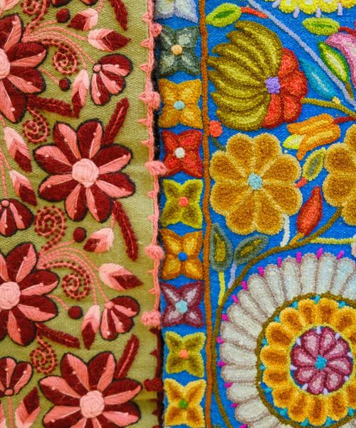 Colorful embroidery featuring intricate floral patterns with pink, red, and yellow flowers on green and blue fabric backgrounds.