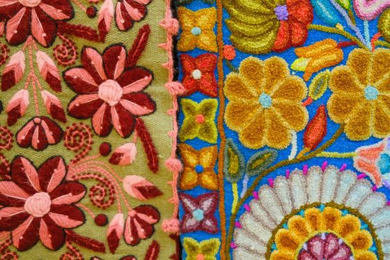 Colorful embroidery featuring intricate floral patterns with pink, red, and yellow flowers on green and blue fabric backgrounds.