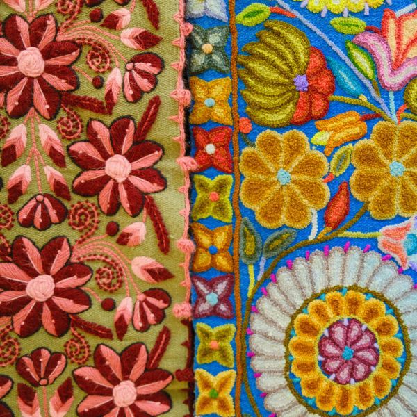 Colorful embroidery featuring intricate floral patterns with pink, red, and yellow flowers on green and blue fabric backgrounds.