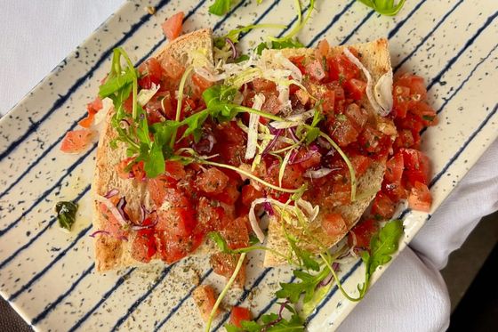 A rectangular plate of bruschetta topped with diced tomatoes, greens, and shredded cheese, placed on a striped surface.