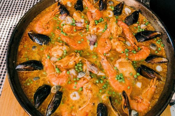 A large pan of seafood paella with shrimp, mussels, peas, and rice on a wooden board, garnished and ready to serve.