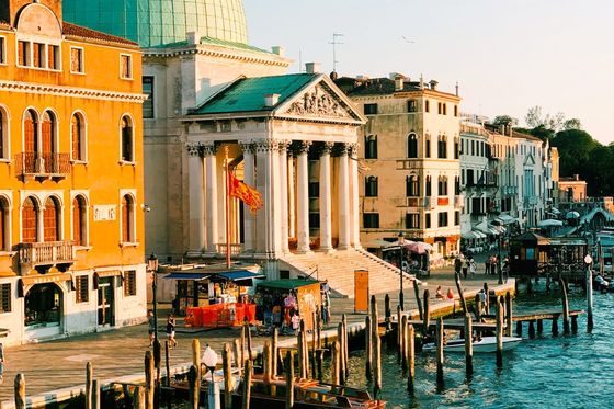 View of Venice canal with moored boats, historic buildings, and a domed church bathed in warm sunlight.