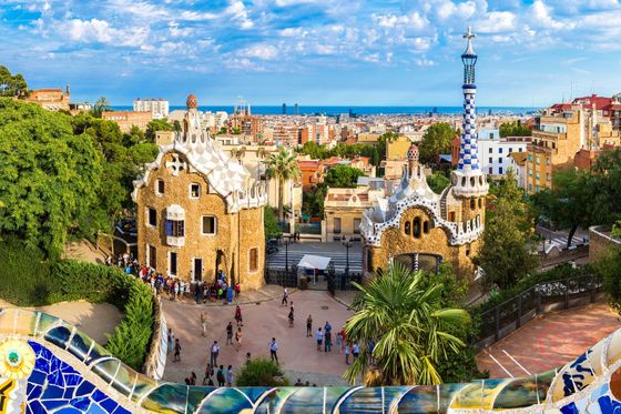 Colorful view of Parc Güell in Barcelona, featuring vibrant mosaic tiles and unique, whimsical buildings under a bright, cloudy sky.