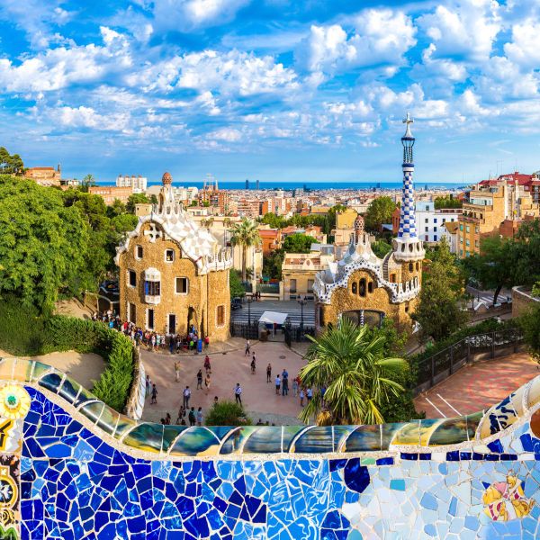 Colorful view of Parc Güell in Barcelona, featuring vibrant mosaic tiles and unique, whimsical buildings under a bright, cloudy sky.
