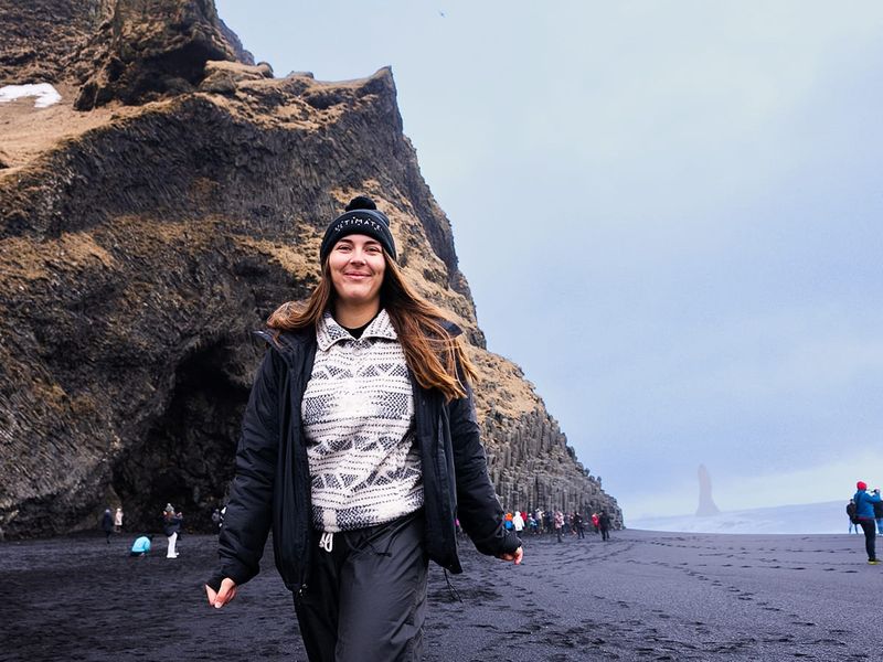 A woman walking on a black sand beach.