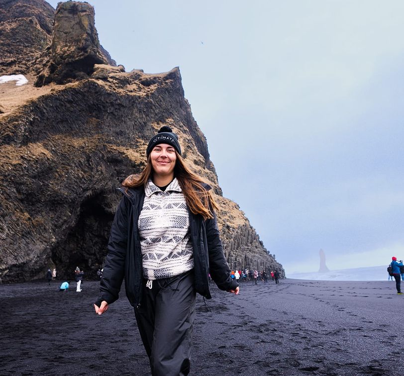 A woman walking on a black sand beach.