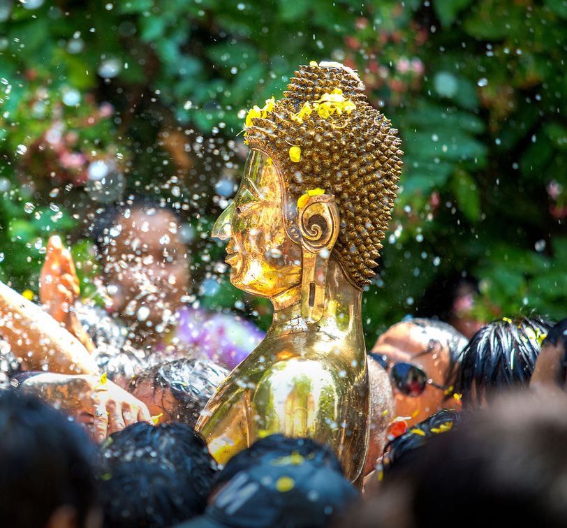 Golden Buddha statue being splashed with water by a crowd during a festive outdoor celebration.