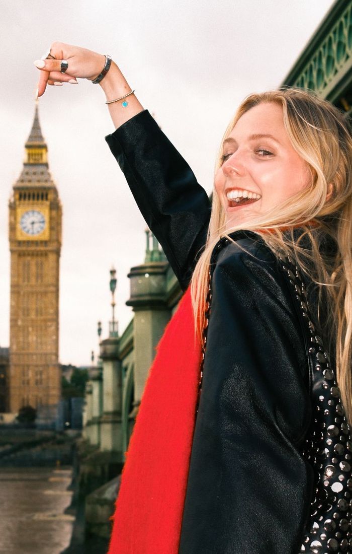Smiling woman in a red scarf gestures towards Big Ben with London Bridge in the background.