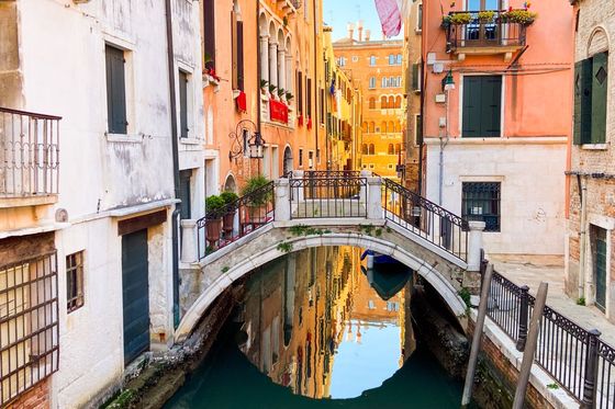Picturesque canal in Venice with arched bridge, colorful buildings, and reflections in the water on a sunny day.