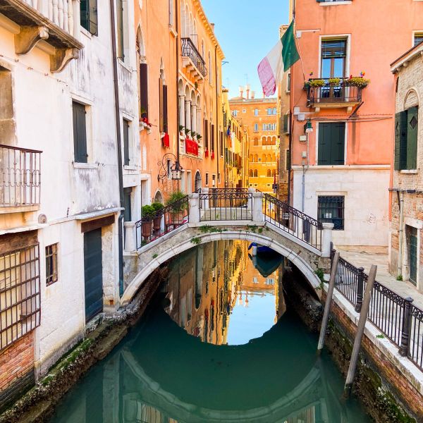 Picturesque canal in Venice with arched bridge, colorful buildings, and reflections in the water on a sunny day.