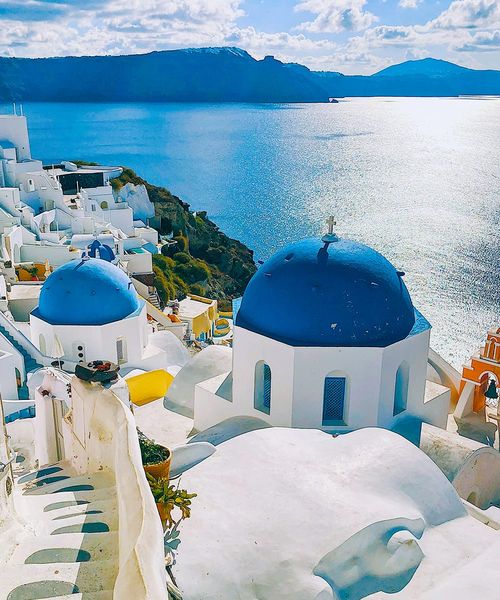 White buildings with blue domed roofs on a cliff overlooking the ocean.