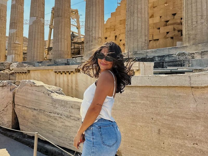A woman posing in front of a stone wall and columns