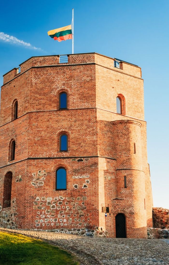 Brick castle tower with narrow windows under a clear blue sky, topped by a flag waving in the breeze.