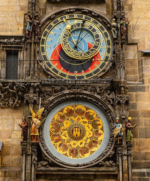 Ornate astronomical clock with colorful dials and intricate figures, set in a stone wall.