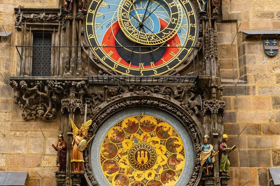 Ornate astronomical clock with colorful dials and intricate figures, set in a stone wall.
