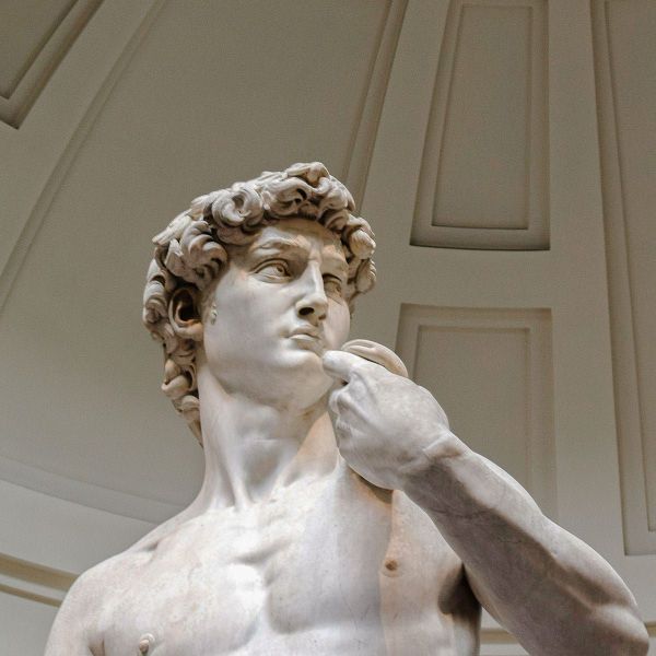 Marble statue of a muscular male figure with curly hair, looking thoughtfully to the side, set against a domed architectural background.