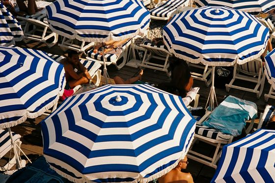 Aerial view of a crowded beach with people lounging under blue and white striped umbrellas on sunbeds.