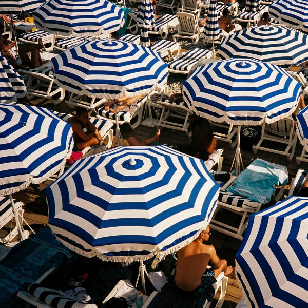 Aerial view of a crowded beach with people lounging under blue and white striped umbrellas on sunbeds.