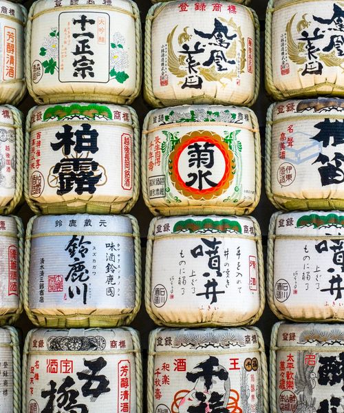 Stacked barrels of sake wrapped in straw with Japanese calligraphy on display.