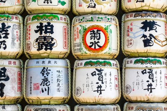 Stacked barrels of sake wrapped in straw with Japanese calligraphy on display.