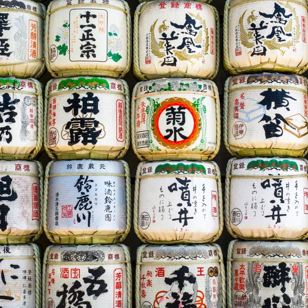 Stacked barrels of sake wrapped in straw with Japanese calligraphy on display.