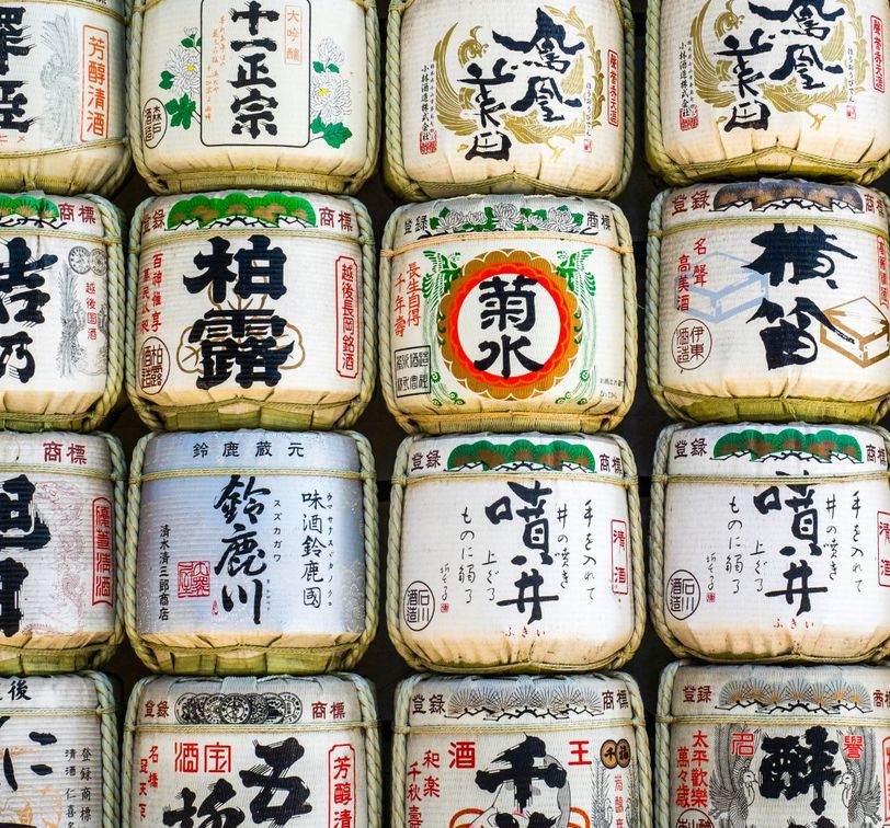 Stacked barrels of sake wrapped in straw with Japanese calligraphy on display.
