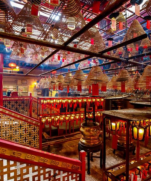 Interior of a temple with numerous spiral incense coils hanging from the ceiling, and red pillars and lanterns enhancing the vibrant atmosphere.