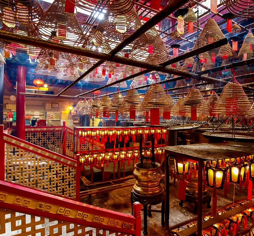 Interior of a temple with numerous spiral incense coils hanging from the ceiling, and red pillars and lanterns enhancing the vibrant atmosphere.