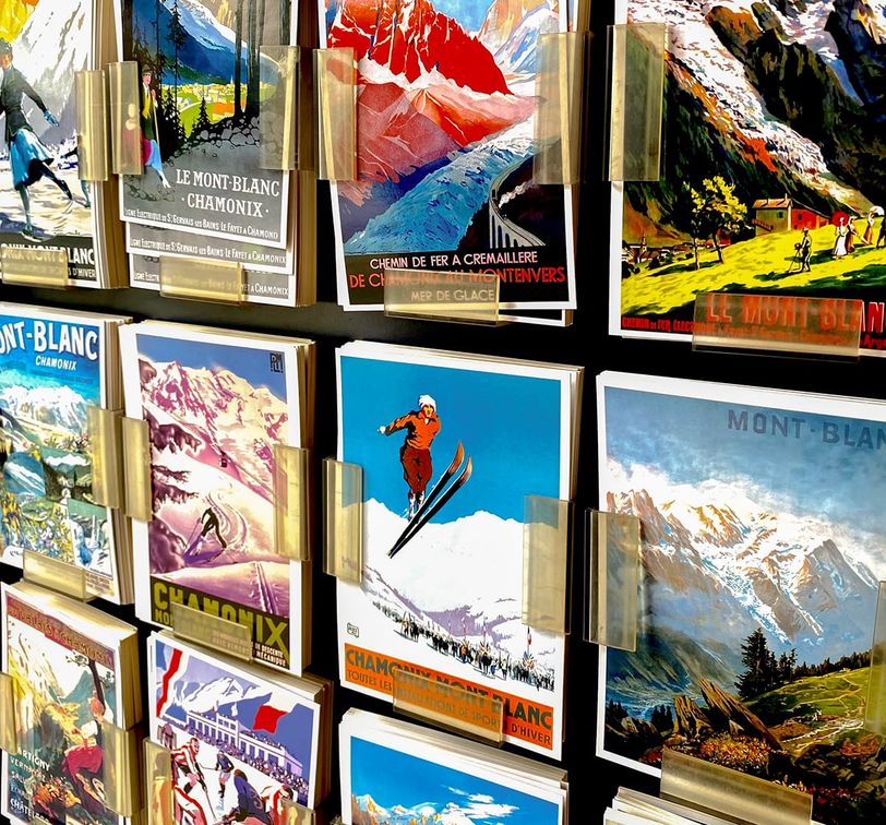 A display of colorful vintage Mont-Blanc ski postcards with scenic mountain images and skiers, held in clear plastic holders on a stand.