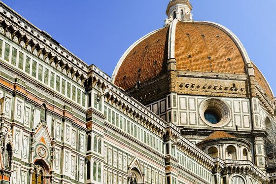 The image shows the Florence Cathedral with its iconic red-tiled dome, intricate green and white marble facade, and a clear blue sky in the background.