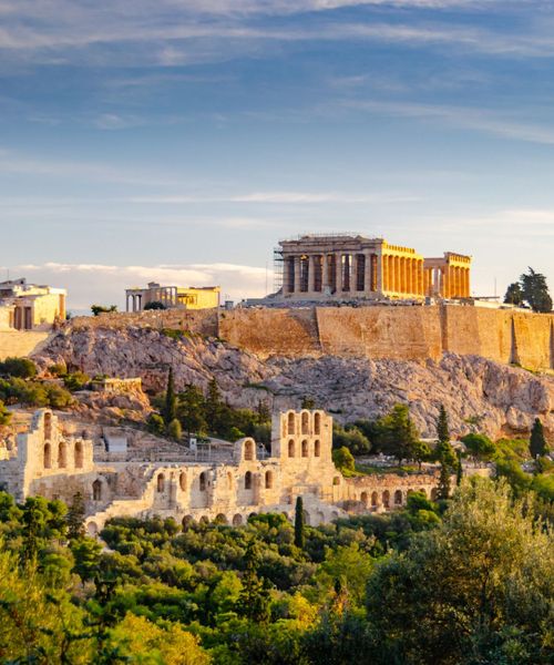 The Parthenon atop the Acropolis in Athens, Greece, bathed in golden sunlight, surrounded by lush greenery and ancient ruins.