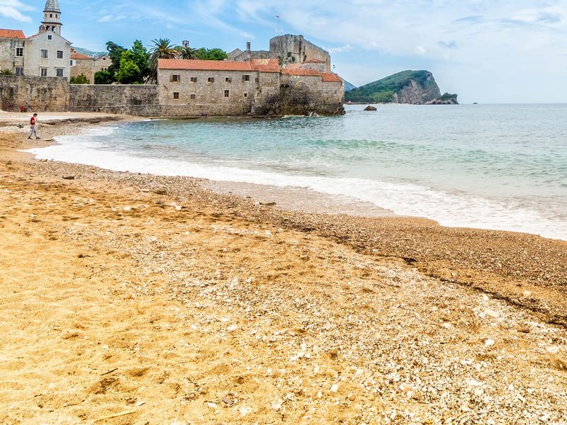 Sandy beach with a distant view of a coastal town, featuring historic buildings and a church tower under a partly cloudy sky.