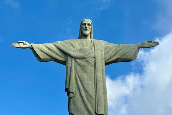 Statue of Christ the Redeemer with outstretched arms against a blue sky with clouds.