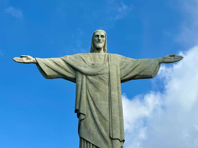 Statue of Christ the Redeemer with outstretched arms against a blue sky with clouds.