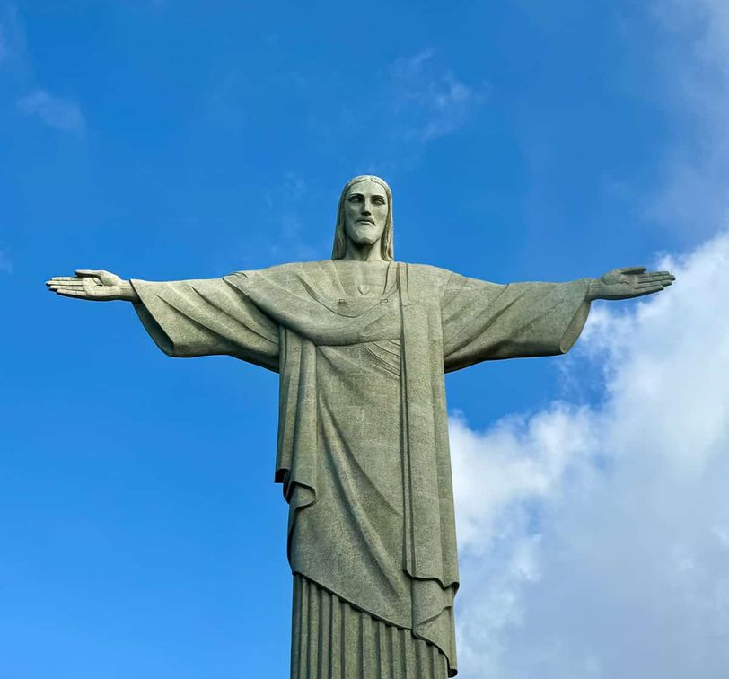 Statue of Christ the Redeemer with outstretched arms against a blue sky with clouds.