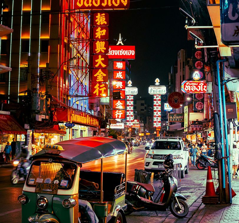 A vibrant street at night with a tuk tuk and cars.